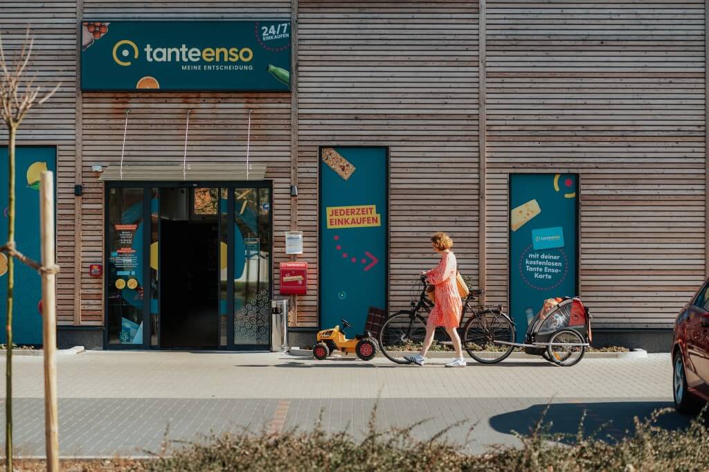 Eine Frau mit Fahrrad und Kinderanhänger stellt ihr Rad vor einem Tante Enso ab.