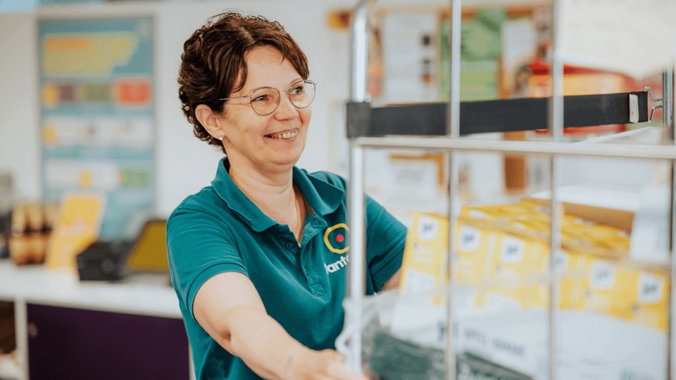 Eine fröhliche Tante Enso-Mitarbeiterin schiebt einen Rollwagen voller Produkte.